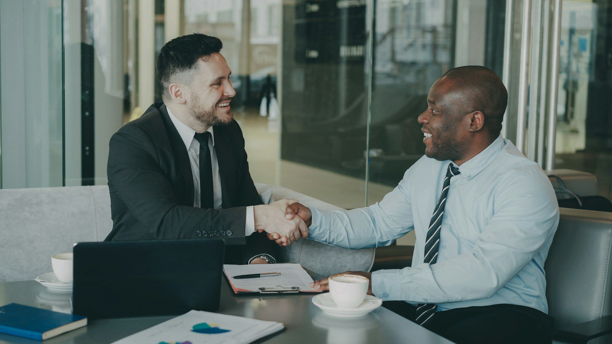 Twee ondernemers geven elkaar een hand aan tafel