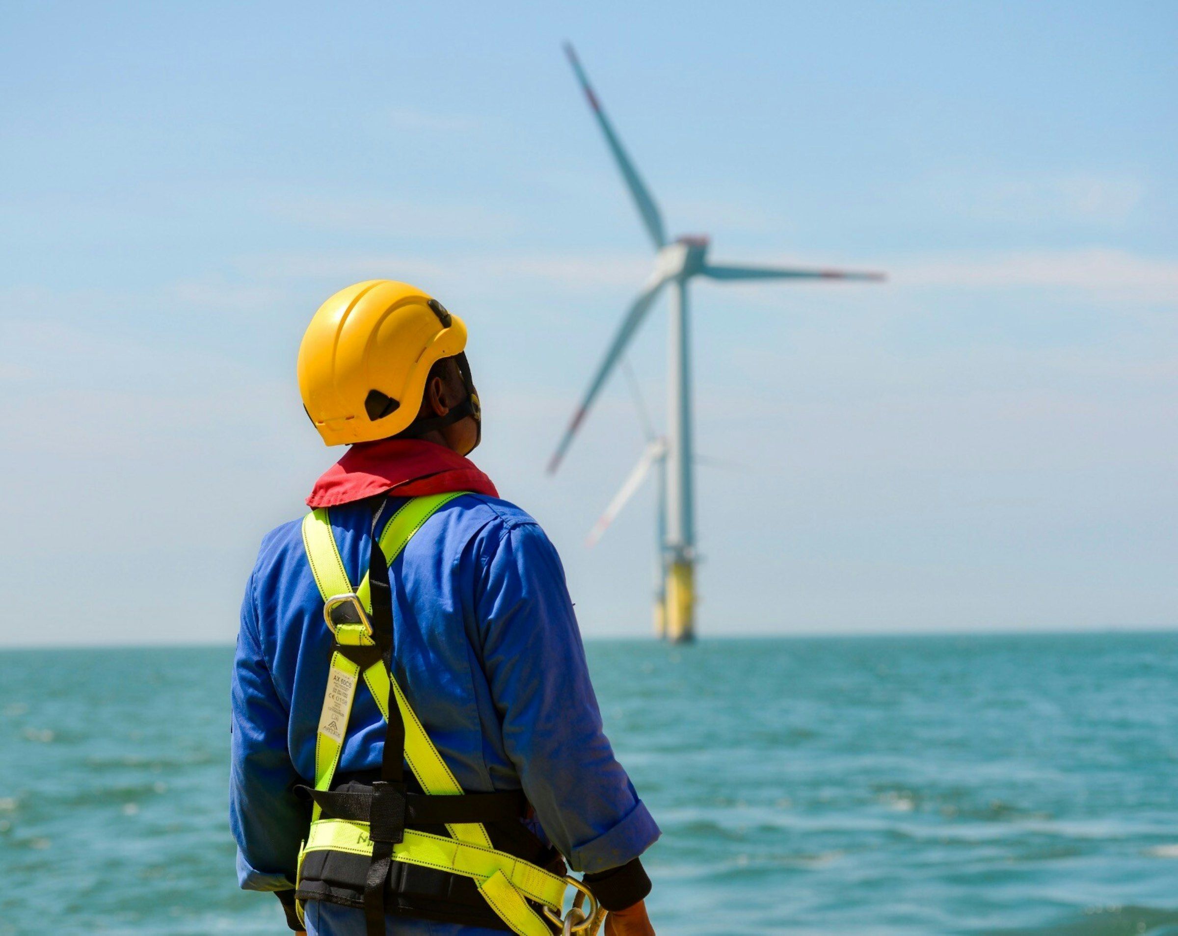 Monteur met helm en valharnas kijkt uit over een windturbine op zee
